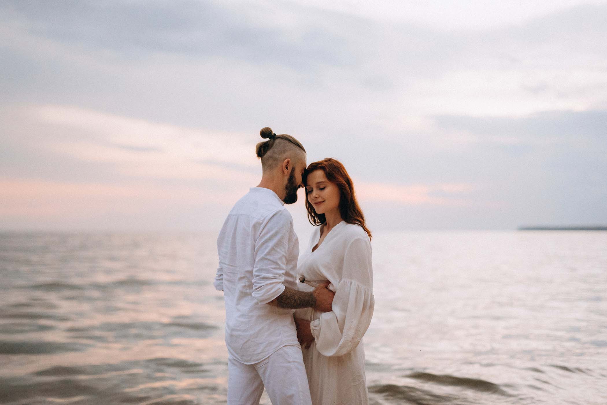 a guy with a girl in white clothes on the seashore next to clay cliffs