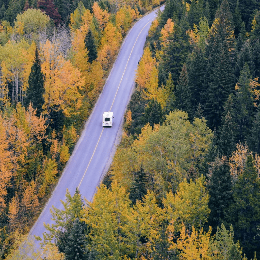 A camper van traveling a long a deserted road with trees